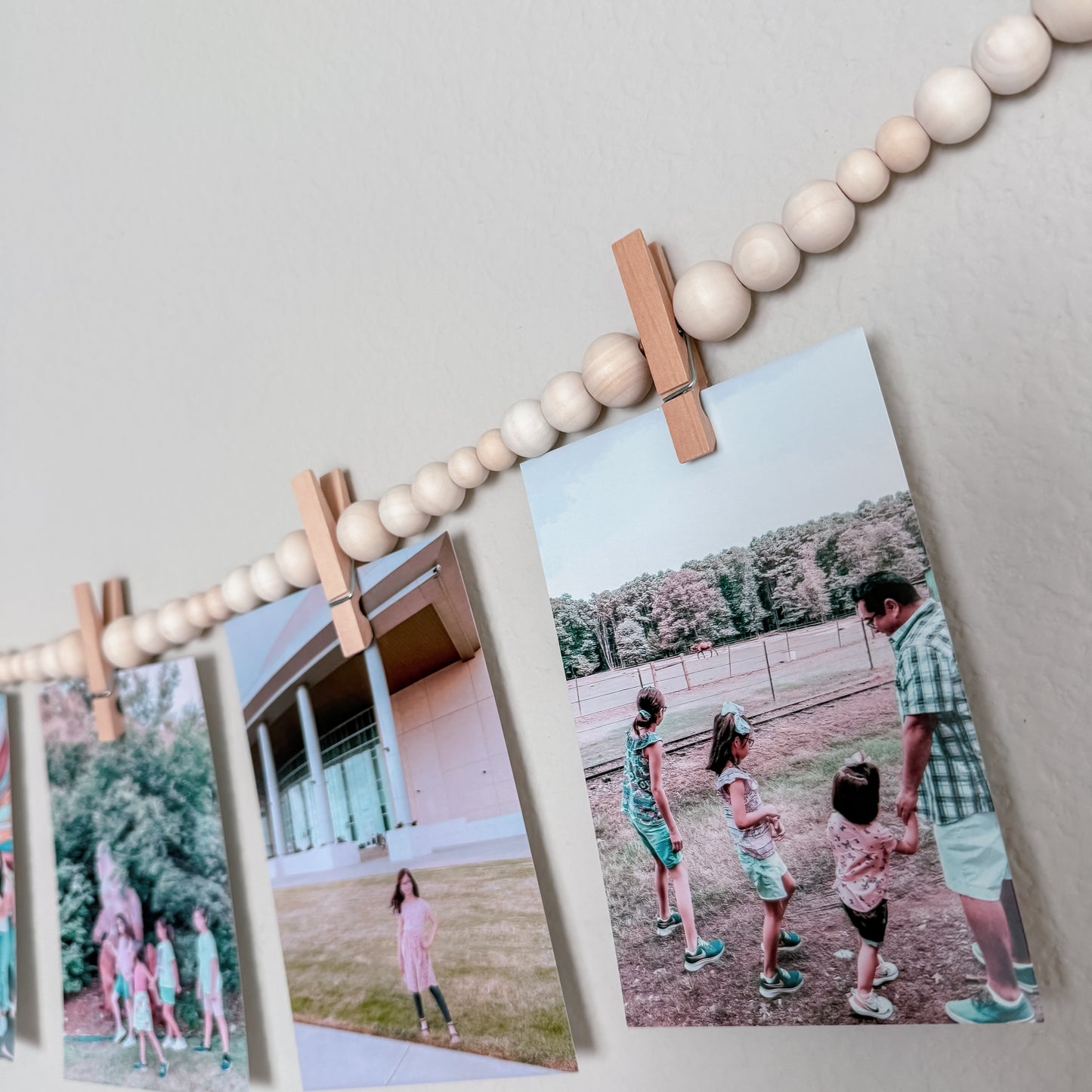 String of wooden beads with clips holding up family photos on a wall.
