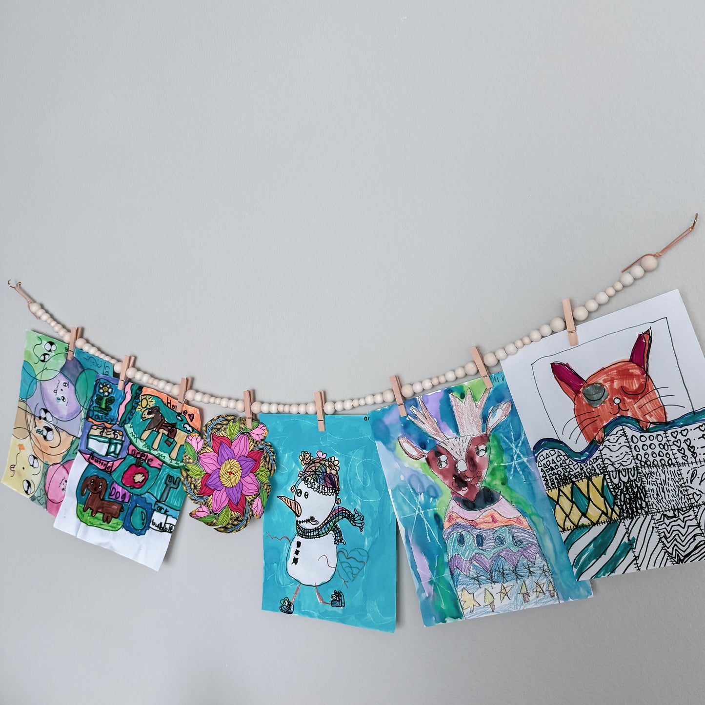 Colorful children's artwork hanging on a line with wooden pegs