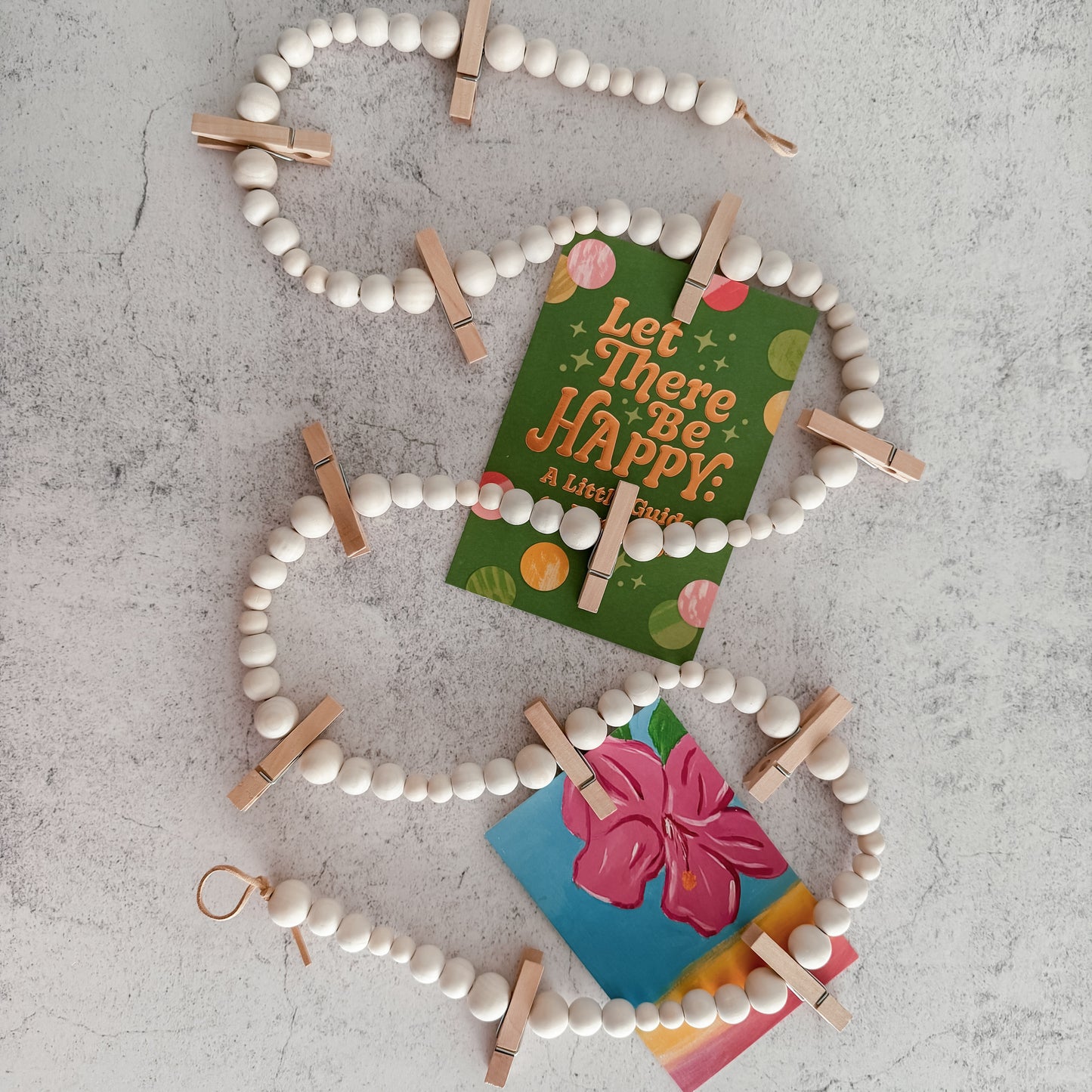 Decorative wall hanging with beige beads and wooden clips holding colorful cards