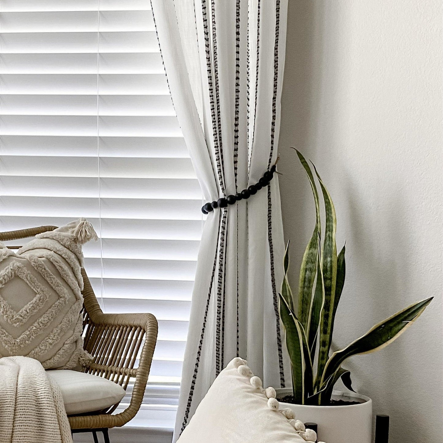 White curtain with black trim in a room with a chair, pillow, and plant.