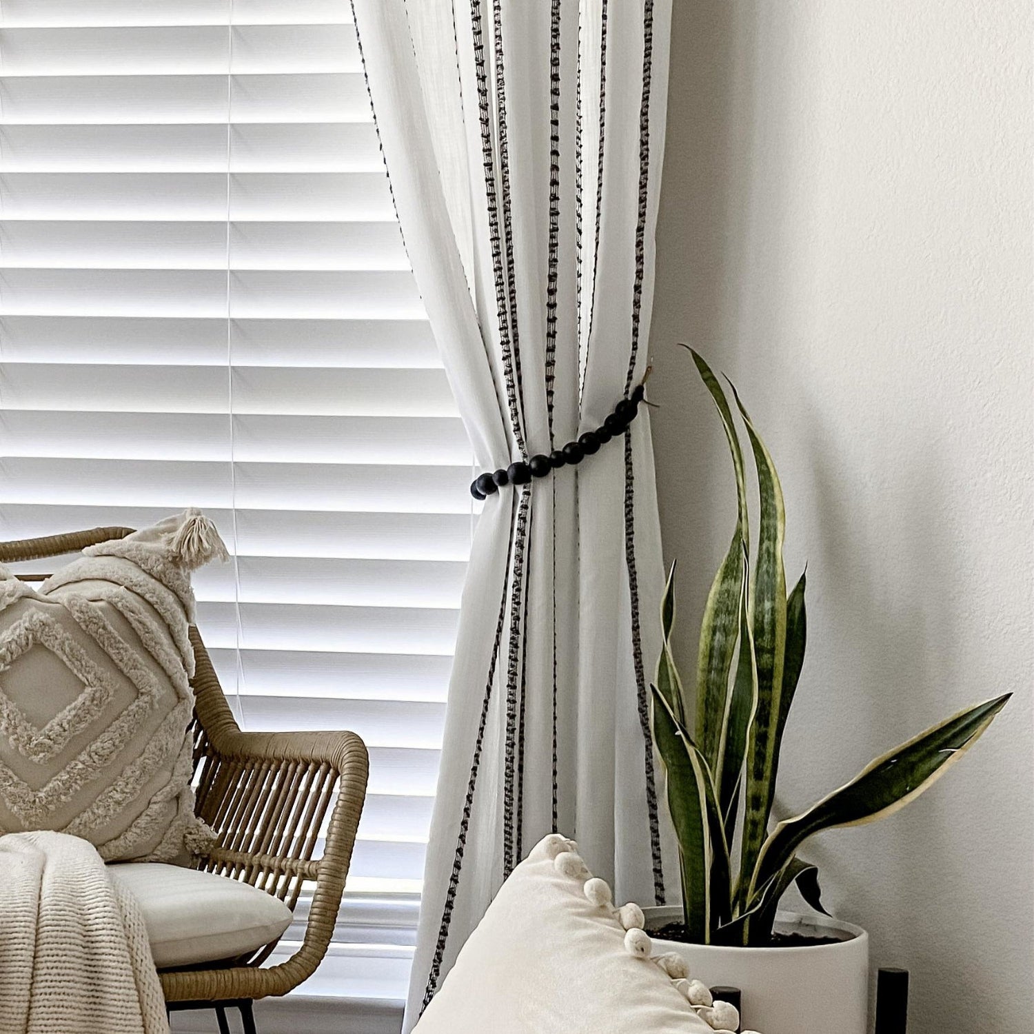 White curtain with black trim in a room with a chair, pillow, and plant.